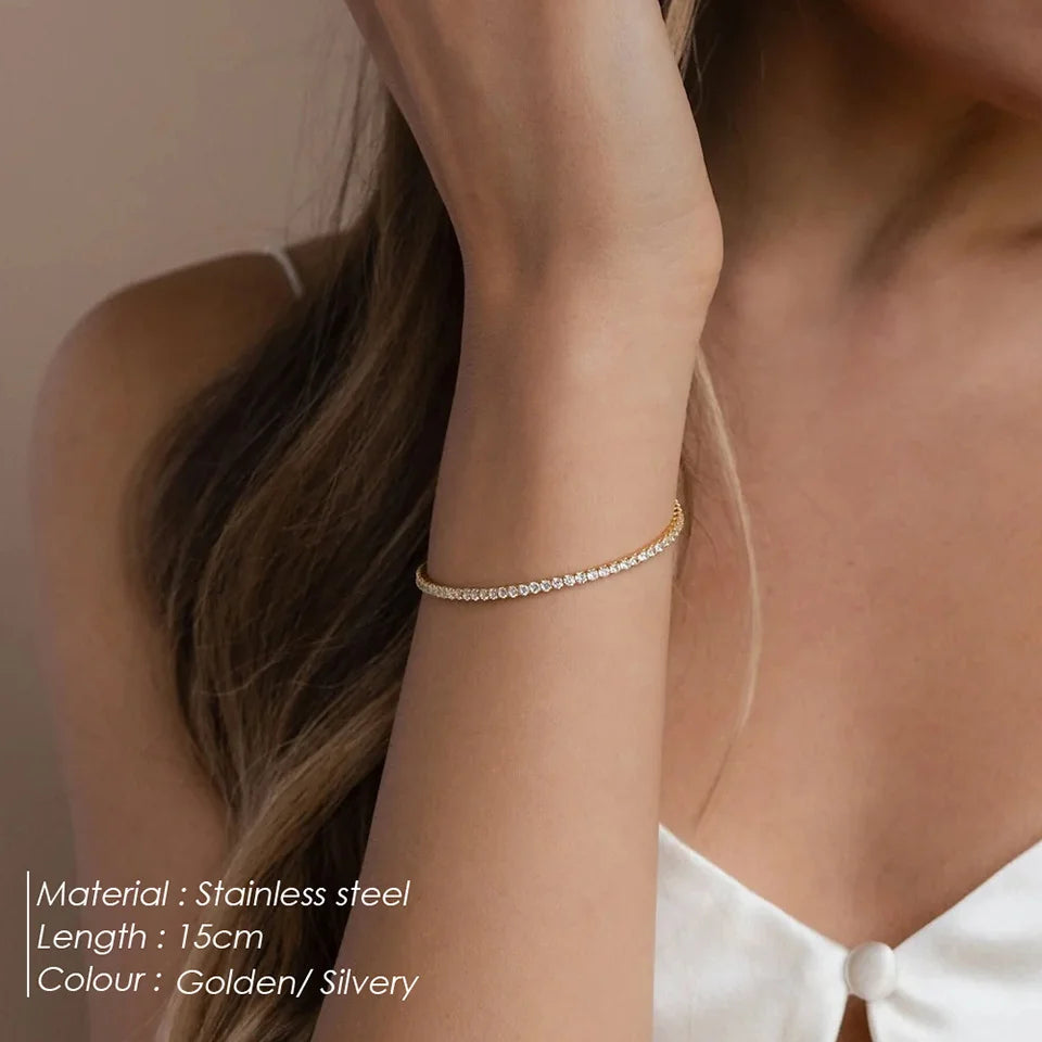 Woman wearing a thin gold-tone tennis bracelet on her wrist, with text listing 15cm length and gold or silver colour