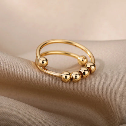 Gold-tone open spinner ring with small sliding beads, resting on beige fabric