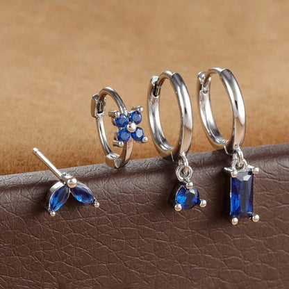Silver-tone four-piece ear stack with blue stones: leaf stud, flower huggie, round drop hoop and baguette drop hoop