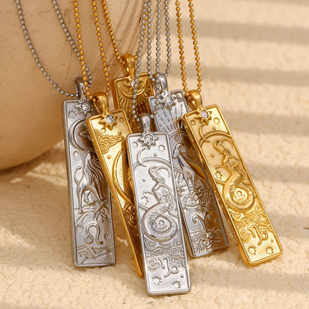 Group of gold-tone and silver-tone zodiac bar pendant necklaces on a beige surface