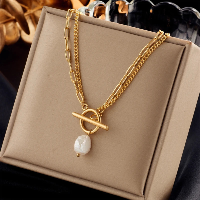 Gold-tone double paperclip chain necklace with front toggle clasp and baroque pearl drop, displayed on a beige box