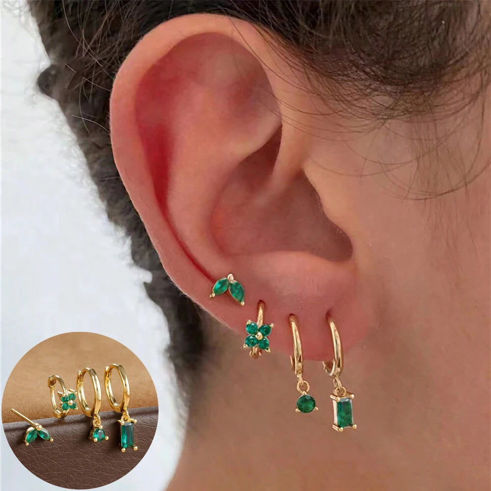 Ear wearing a gold-tone stack of green-stone leaf stud, flower huggie and two drop hoops, with inset of the set