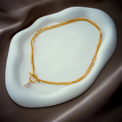 Gold-tone layered paperclip chain necklace with toggle clasp and small pearl drop, on a pale blue trinket dish