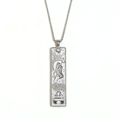 Silver-tone Libra zodiac bar pendant necklace with engraved figure and scales symbol, and a small clear stone, on white