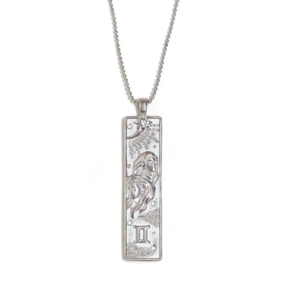 Silver-tone Gemini zodiac bar pendant necklace with engraved twins and a small clear stone, on white