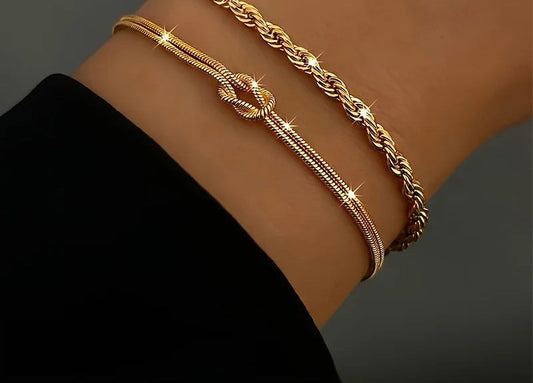 Two gold stacking bracelets, a knotted snake chain and a rope chain, on the wrist
